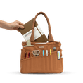 Load image into Gallery viewer, A hand is holding a brown leather tote bag with various office supplies and a notebook inside.
