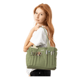 Load image into Gallery viewer, A young woman with red hair is standing against a black background, wearing a white shirt and carrying a green bag with various items in it.